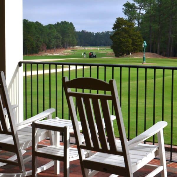 View of the Pinehurst Country Club with a golf cart and golfers from the porch with rocking chairs.