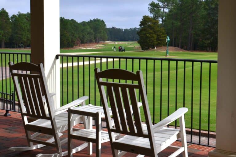 View of the Pinehurst Country Club with a golf cart and golfers from the porch with rocking chairs.