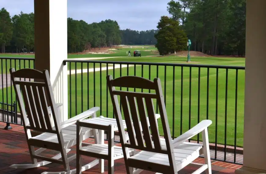 View of the Pinehurst Country Club with a golf cart and golfers from the porch with rocking chairs.