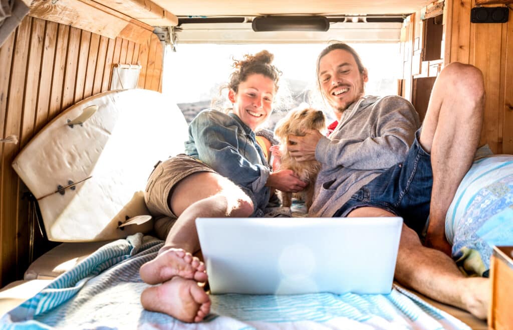 Digital nomad couple with cute dog using laptop on retro mini van transport